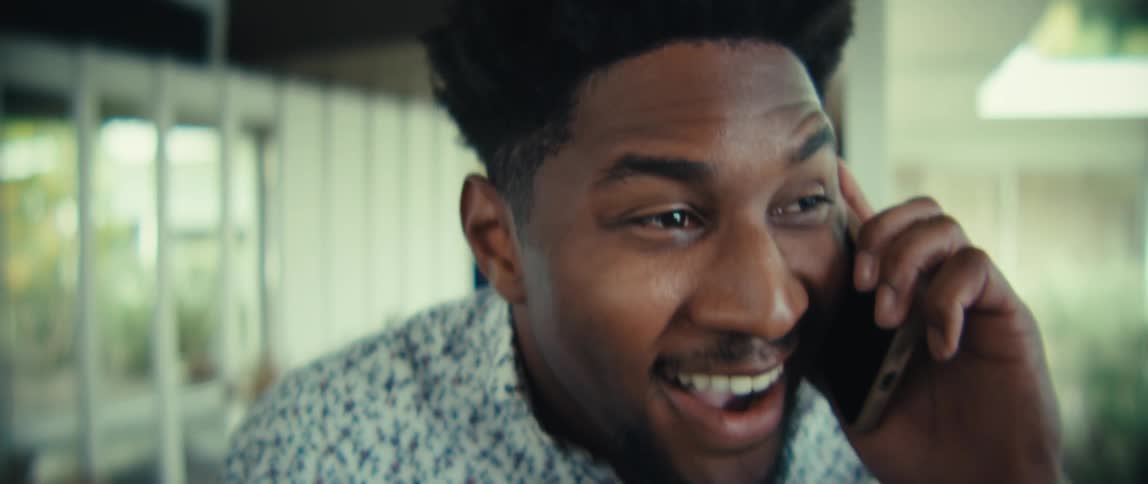 Man hanging his jacket in an airy decorated home smiles and laughs while answering a smartphone call