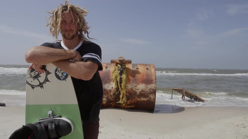 Man stands with wake board on sunny beach on windy day