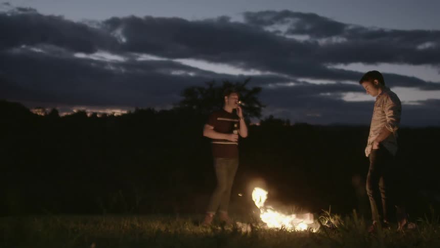 Two men standing by a campfire at night