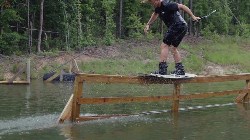A man wakeboards over wood rails in a lake