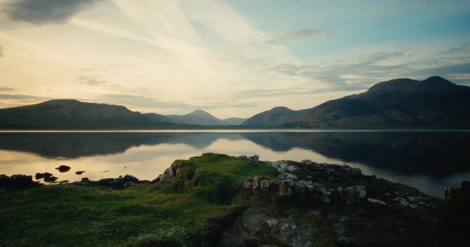 A lake with a mountain range in the background viewed from an island at sunset