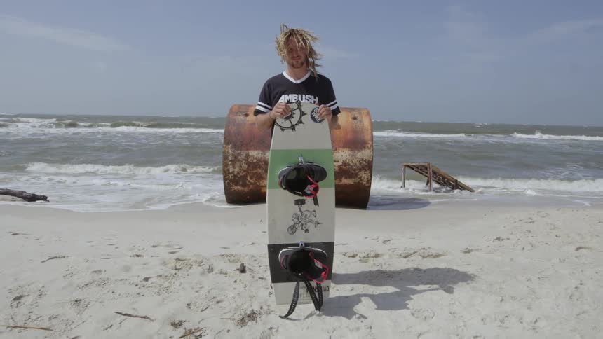 A surfer stands on the beach holding his surfboard