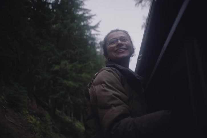 Woman with her head out of the window of a moving car through a forest