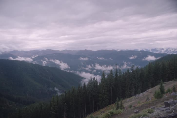 A cloudy day on a highland with forested areas and a mountain range in the background