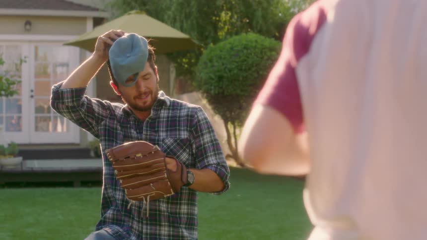 A man plays catch with a boy in a sunny backyard