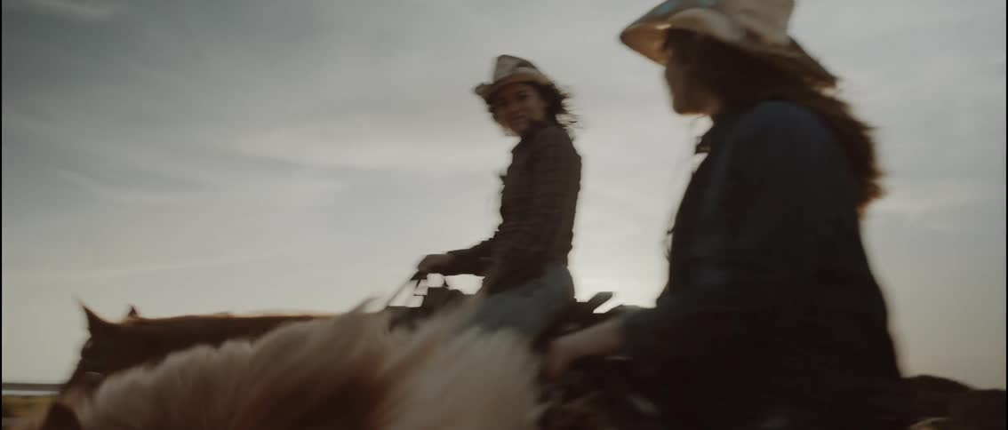 Young adult woman and teenager girl wearing cowboy hats and plaid shirts riding horses outdoors during dusk or dawn