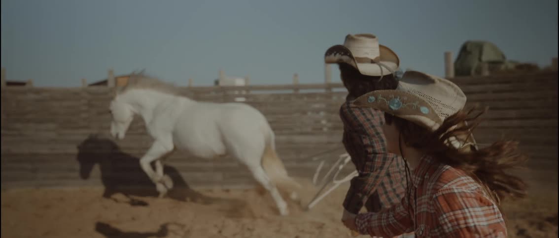 A woman and her daughter chasing a horse around a corral