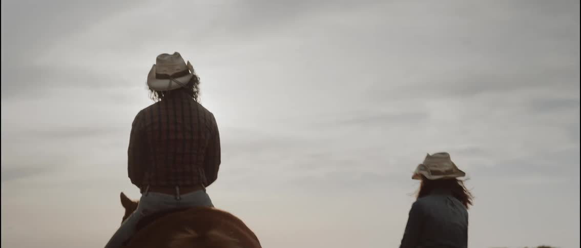 A woman and her daughter sitting on horses in an outdoor arena watching the sunset