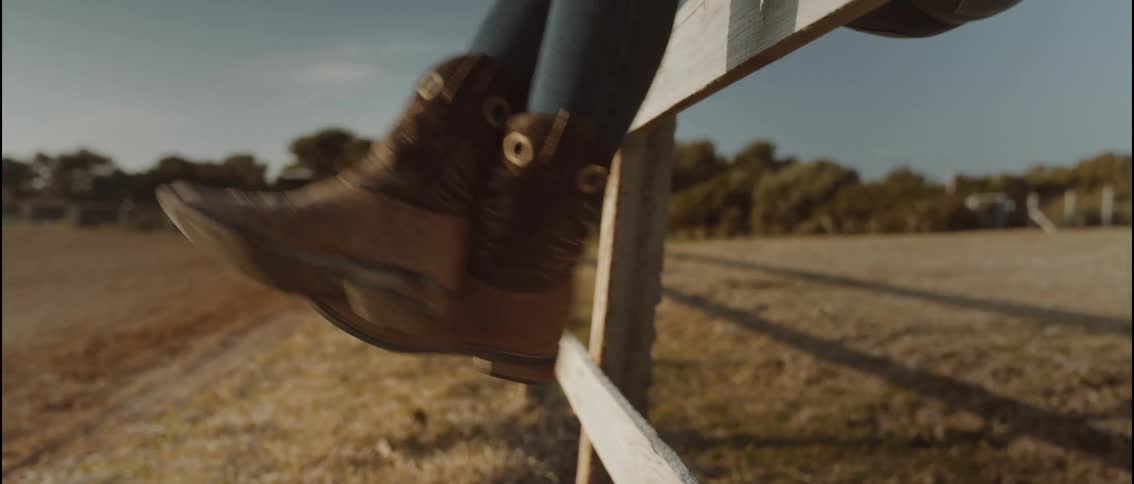 Brown boots resting on a wooden fence in a rural area