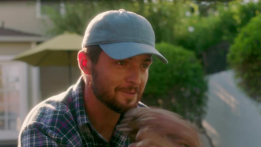 A man puts on a baseball cap while holding a baseball and mitt