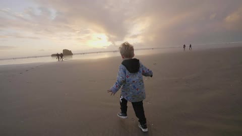 A boy runs along the sand of a beach on a cloudy day at dusk
