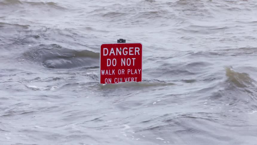 Red warning sign partially submerged in rough water