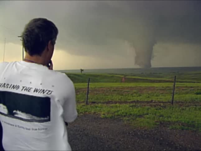 The man is taking photographs of a tornado in the distance