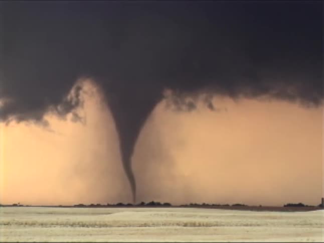 Tornado forming beneath dark clouds over a flat landscape at dusk