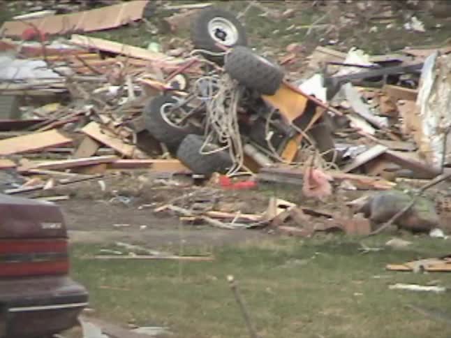 A handheld camera pans across a neighborhood showing houses destroyed and debris scattered by a tornado