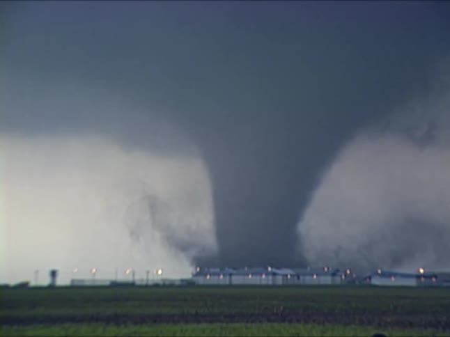 Large tornado moving across farmland with buildings in the background