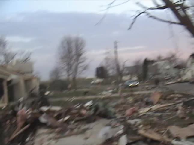 The aftermath of a devastating tornado in a residential neighborhood showing houses leveled and debris scattered across yardsdowned trees pink insulation and shattered wood fill the landscape as the camera pans across the wreckage of multiple homes