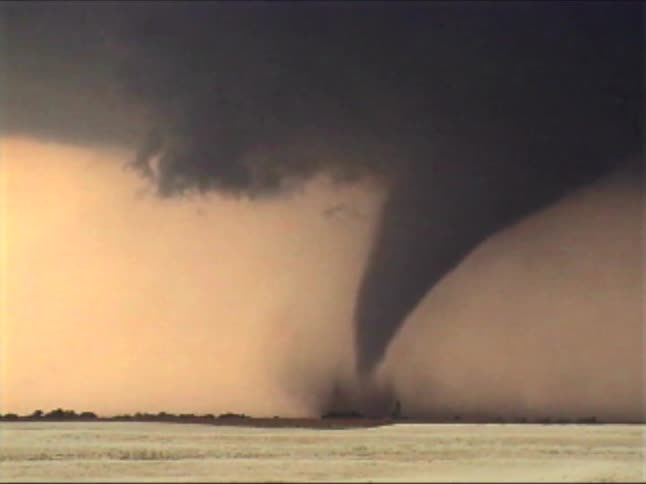Tornado touching down beneath dense clouds over a flat landscape at dusk