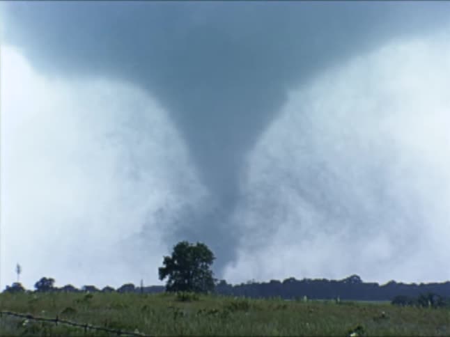 A tornado forcefully spins as it passes over rural grasslands
