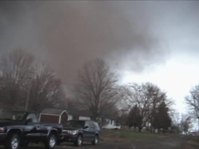 Dog running next to a person in a neighborhood yard with a huge tornado on the ground in the distance