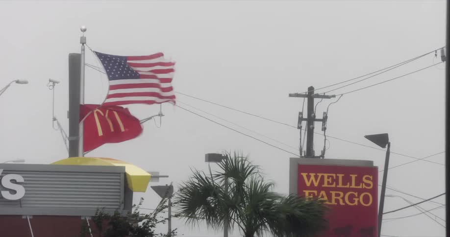 United states flag and mcdonalds flag blowing in the wind near commercial signs and power poles