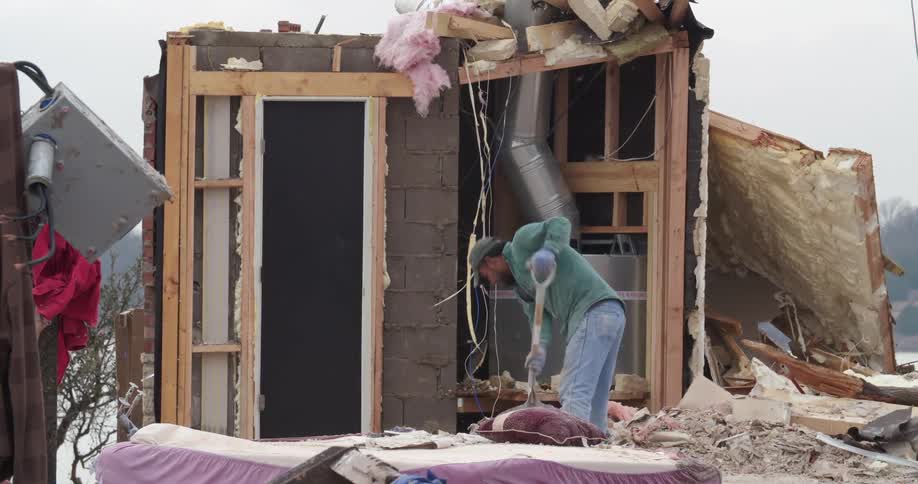 Man removes debris inside a partially destroyed residential structure with exposed insulation