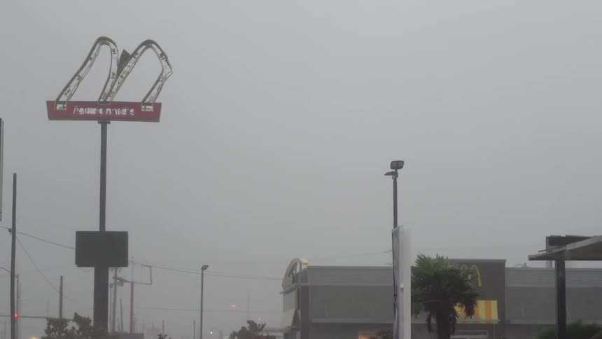 Bent and destroyed mcdonalds sign moves in the strong wind as trees bend and rain falls during a strong storm