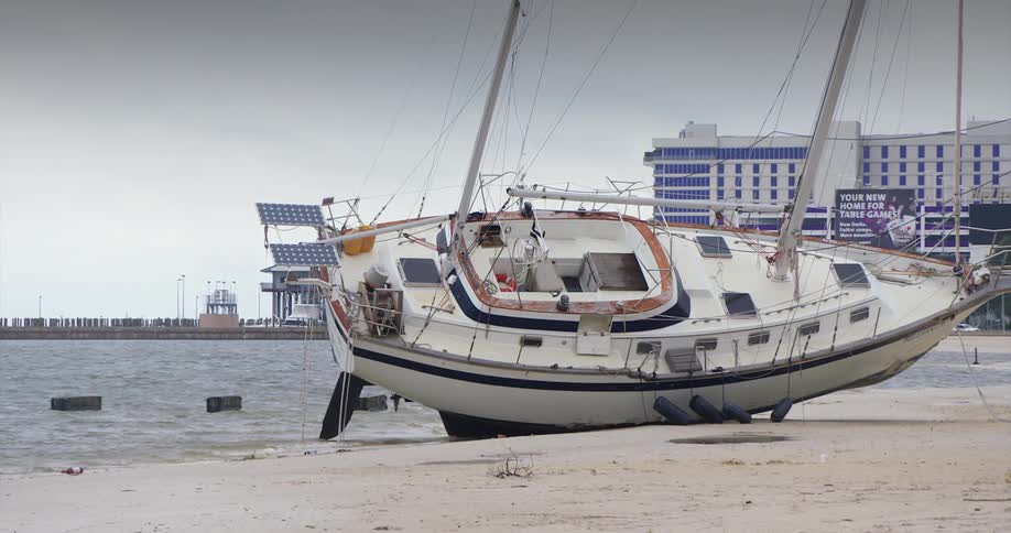 A boat rests on the sandy beach with buildings in the background at midday