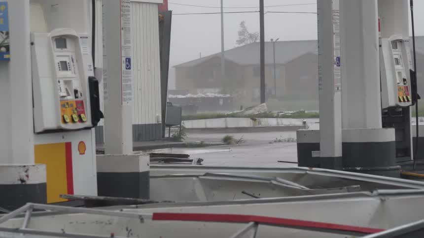 Torrential rain from a hurricane cause to debris to land between standing fuel pumps before a rapid zoom reveals the twisted wreckage of a metal canopy collapsed across the lot