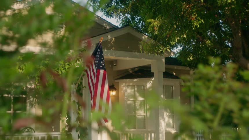 American flag hanging from a front porch of a small house