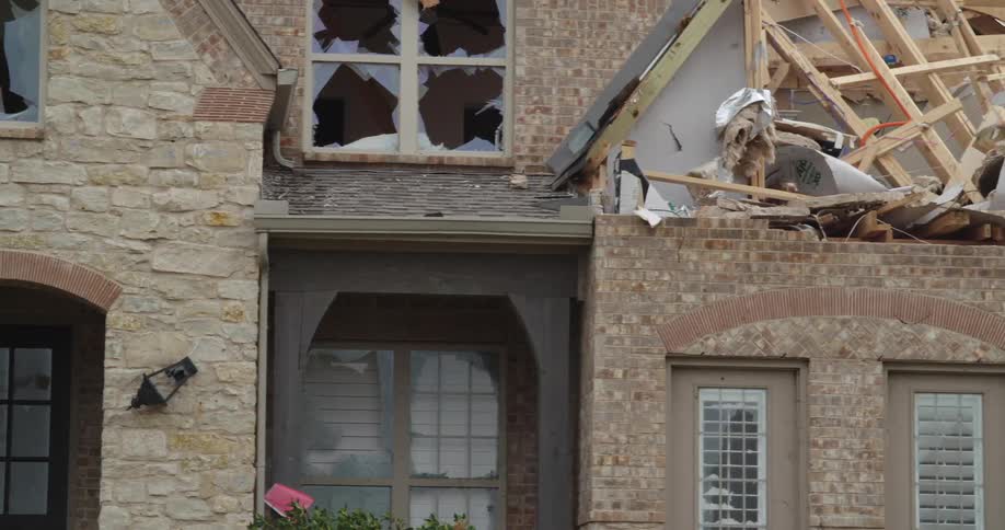 The video captures the extensive damage to a brick house after a severe stormthe roof is partially collapsed exposing wooden beams and insulation while several upstairs windows are completely shattered