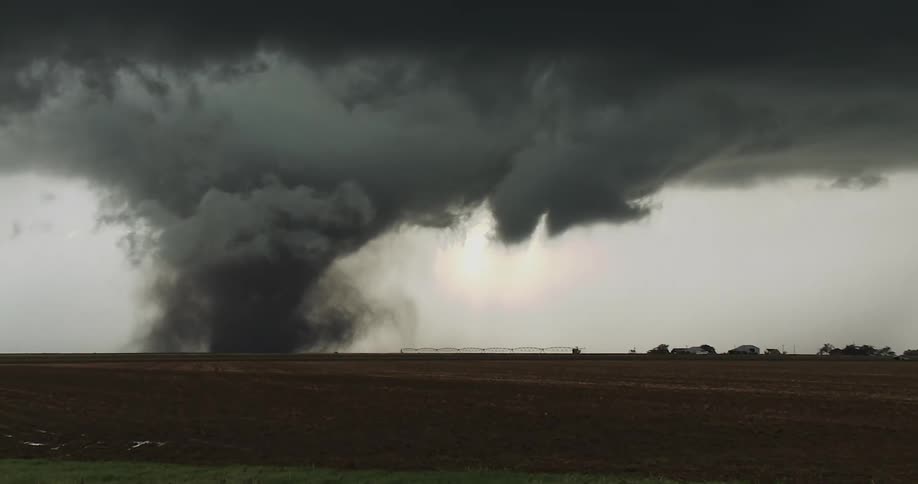Wide tornado beneath dark clouds moving across farmland