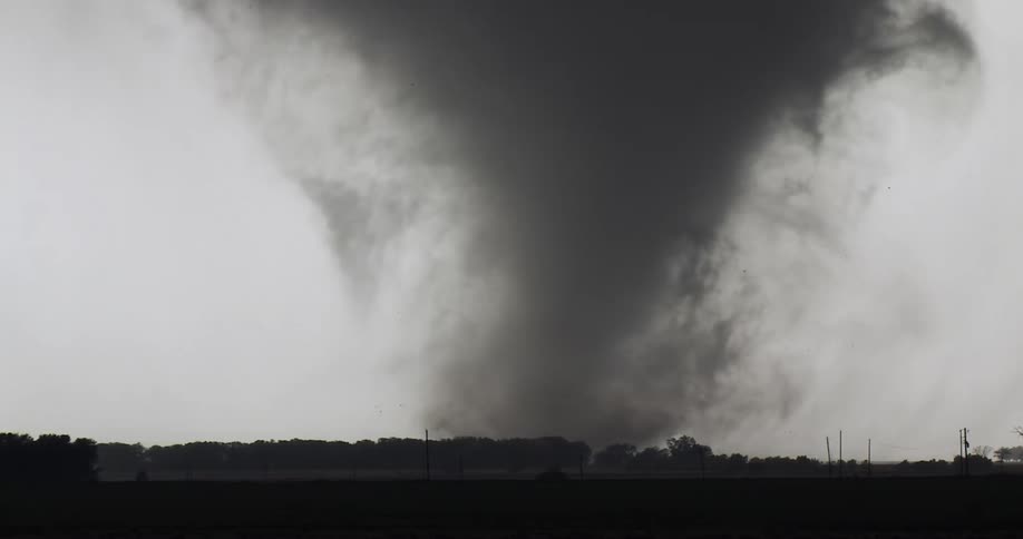 Large tornado with a debris cloud over a tree line in a rural area