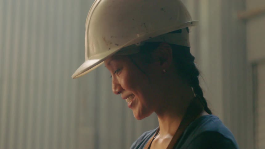 Smiling asian woman wearing a hard hat at a work site