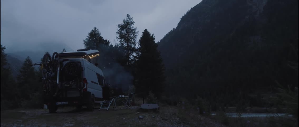The van with fairy lights is parked on a camp site in the mountains in the dusk