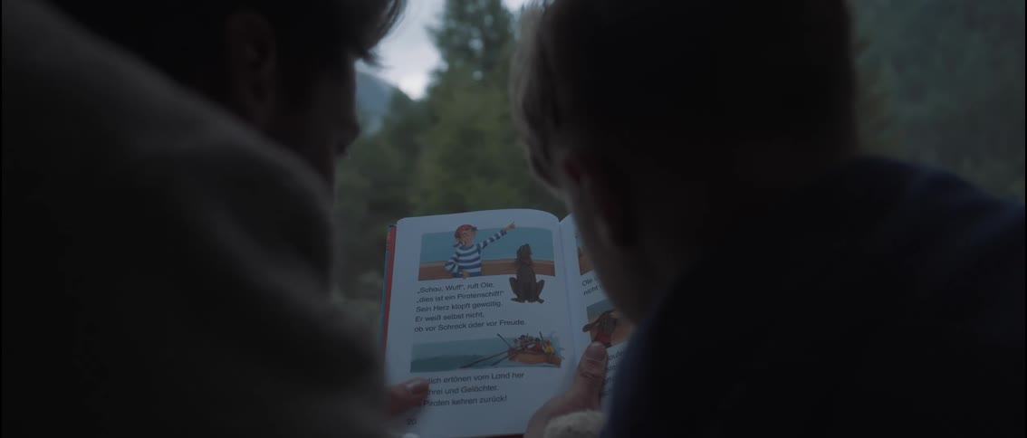 A person reads an illustrated childrens book to a child in the pop-up roof of a Van