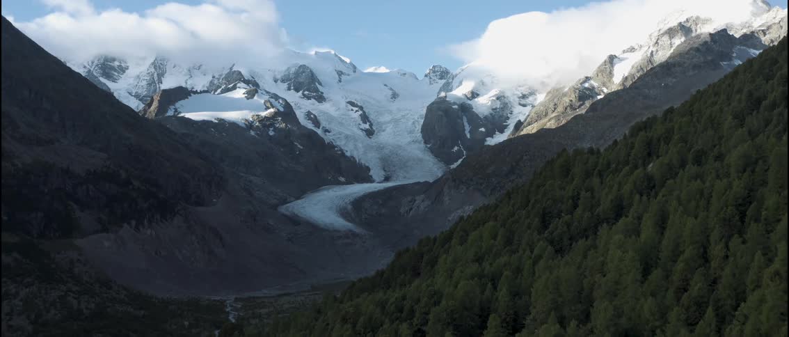 A winding river cuts through a dense mountain forest as it flows between treelined banks the water gliding steadily through the valley while the surrounding greenery stretches across the rugged terrain
