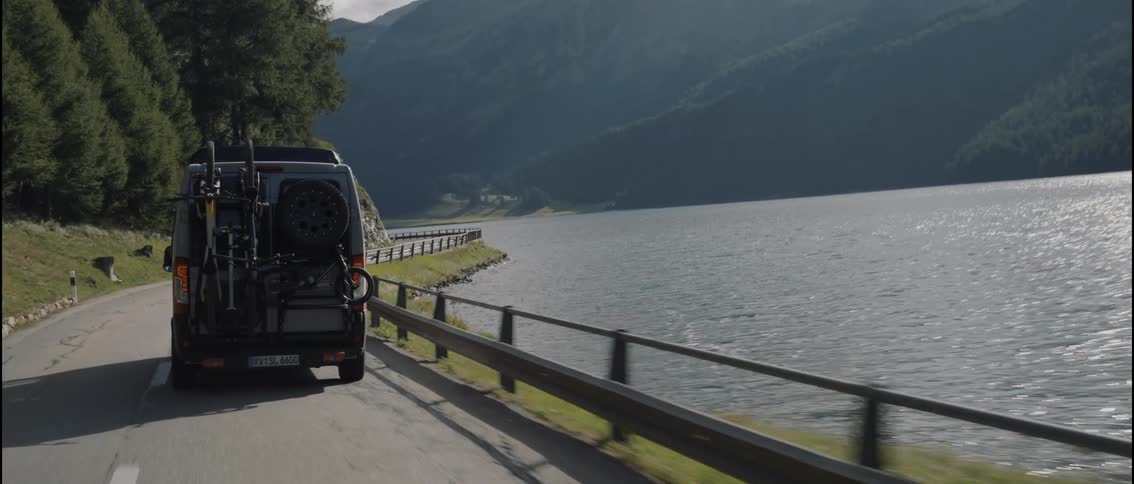 A travel van drives along a road that passes next to a large lake