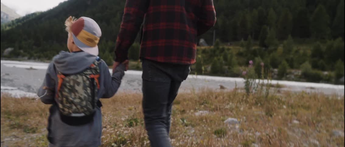 Adult man and young boy walking while holding hands on a field with mountains on the background outdoors during day time