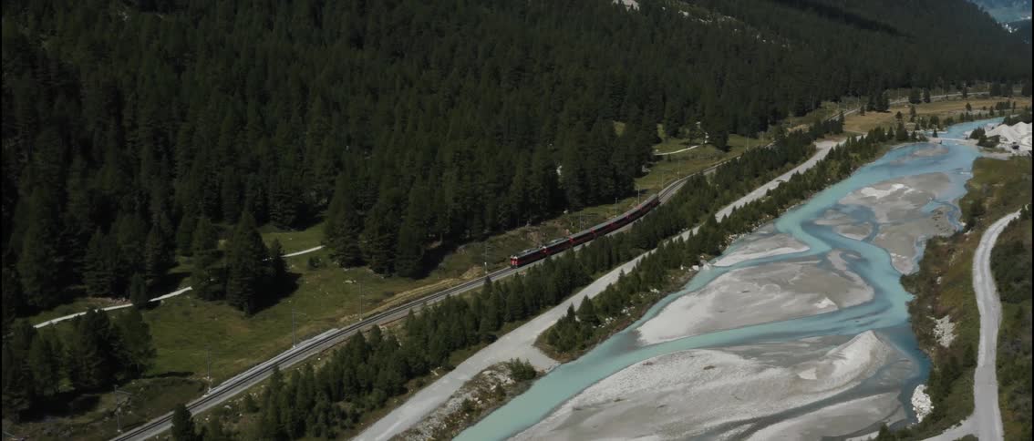 The glacier express train moving along the frozen river in the forested swiss alps mountain valley