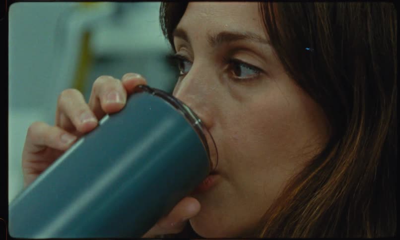A woman with long brown hair takes a sip from a metal tumbler her gaze focused thoughtfully off to the side