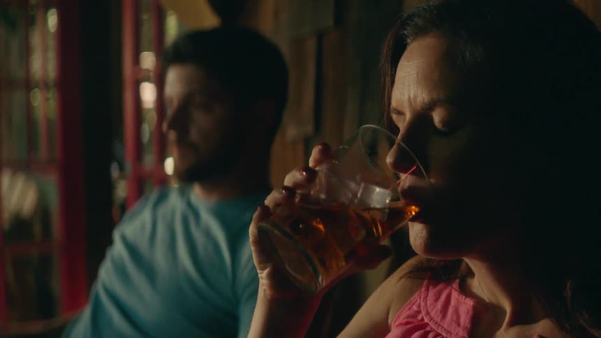 A woman sips iced tea on a porch next to a man