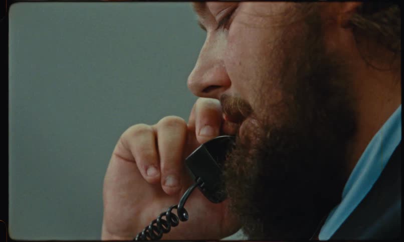 A man in a dark suit reaches for a black polycom desk phone a small orange sticky note is attached to the top of the device