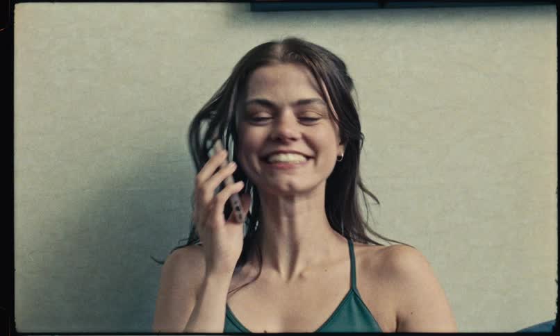 Woman smiling while talking on a mobile phone in front of a lightcolored wall
