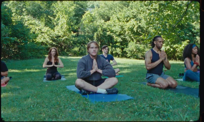 A man struggles to concentrate while meditating during an outdoor yoga class