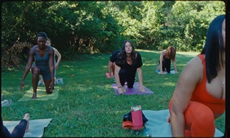 Group of people practicing yoga outdoors on grass with an instructor standing in front