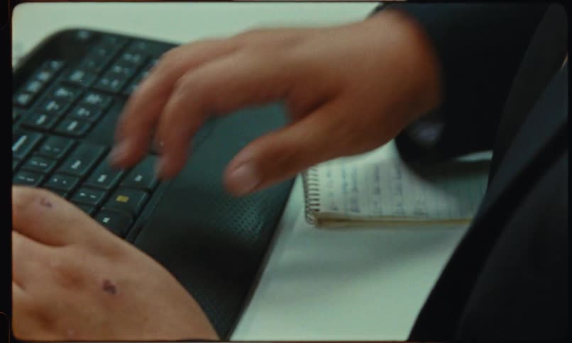 A male worker types on a keyboard before writing on a small notepad