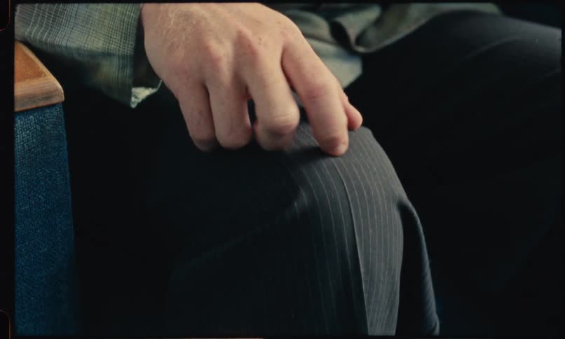 A mans hand resting on and then nervously clutching his pinstriped trouser leg