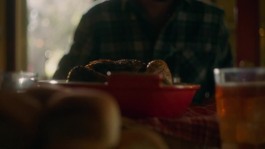 Woman sets cooked chicken on dinner table and man takes a drink