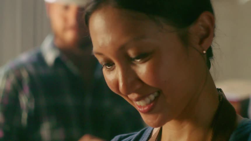 A man approaches a smiling woman from behind